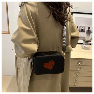 Lifestyle shot of black camera bag with red heart and geometric wide strap on khaki coat