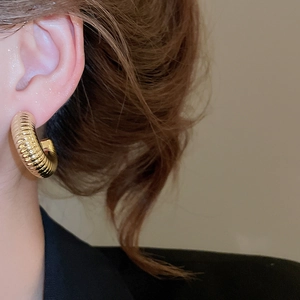 Detailed close-up of golden ribbed C-shaped earrings with fine textured finish