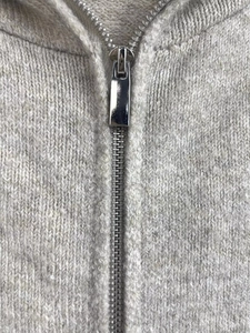 Detailed macro view of high-quality silver metal zipper on gray knit cardigan fabric