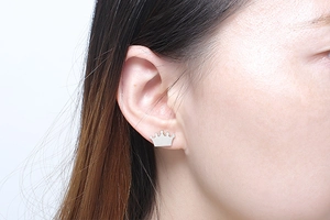Close-up of a silver crown stud earring on a female ear with a minimalist metal design