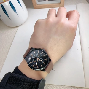 Classic black dial sports watch with brown silicone strap worn on wrist against books