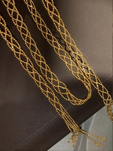 Macro view of woven golden bead necklace showing intricate hollow diamond patterns