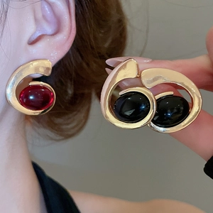 Detail of luxury gold resin earrings featuring oval red and black gemstones in swirl design