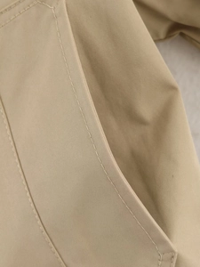 Close-up of khaki trench coat showing precision double-needle stitching on pocket edge