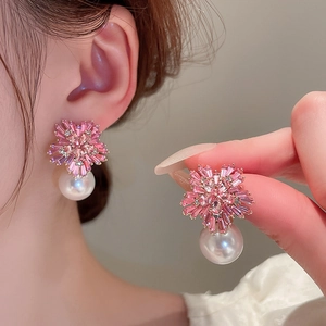Detailed view of flower earrings with pink zircons and hanging white pearl on golden base