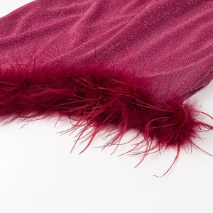 Detail of shimmering magenta dress fabric with soft feather fringe trim on white backdrop