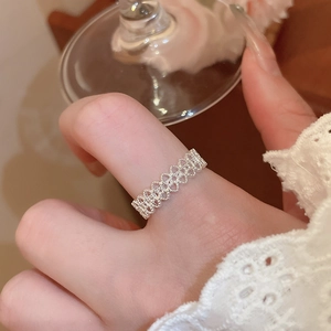Detail of silver heart cutout ring worn by model holding glass for elegant style