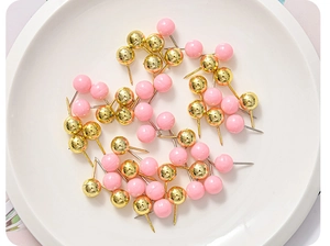 Close-up of pink and gold push pins scattered in a white dish for office desk decor