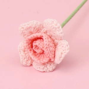 Close-up of handmade pink knitted yarn rose with detailed gradient texture and green stem