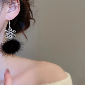 Detail of acrylic snowflake and black pom-pom earring on model with warm tones