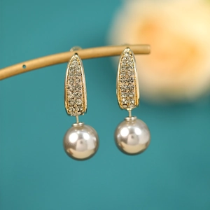 Macro shot of gold tassel earrings with grey pearls and crystal pave on blue background