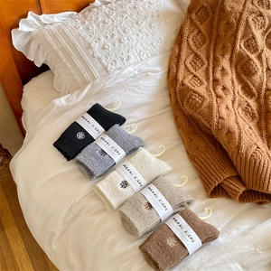 Five pairs of thick winter socks in neutral tones displayed on a cozy white duvet