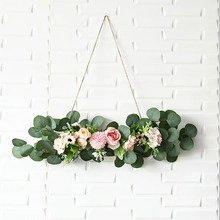 Hanging wall decor featuring pink roses and green eucalyptus leaves on a rustic rope