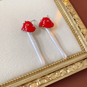 Macro detail of red mushroom pearl earrings in a vintage gold frame on velvet
