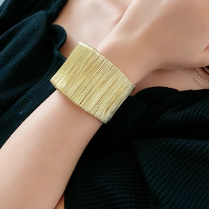 Dettaglio ravvicinato di un ampio bracciale in metallo dorato testurizzato sul polso