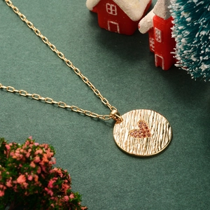 Collier doré avec pendentif rond à texture ondulée et cœur rouge sur fond vert foncé