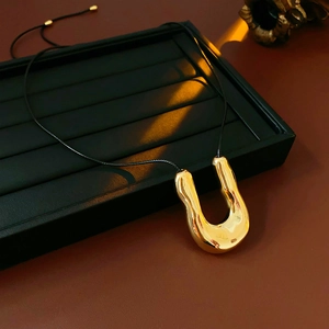 Vue détaillée du pendentif en forme de U en métal liquide doré sur un cordon noir fin