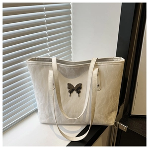 Close-up of white textured tote bag featuring a decorative silver butterfly metal accessory