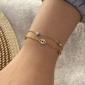 Gold double-layer bracelet with evil eye and heart charms worn on a wrist