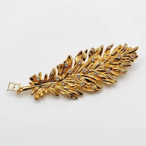 Elegant gold feather brooch featuring sparkling rhinestones on a white background