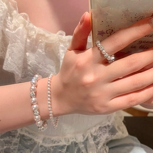 Gros plan sur l'ensemble bracelet en perles et bague porté sur une robe en dentelle