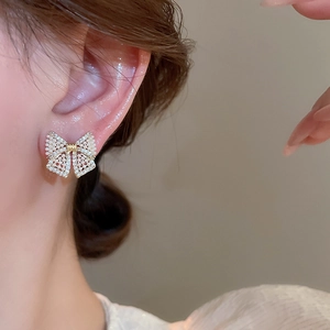 Macro shot of bow knot stud earring with inlaid diamonds and white pearls on ear