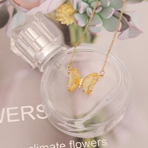 Detail of yellow crystal butterfly pendant with gold chain on artistic floral background