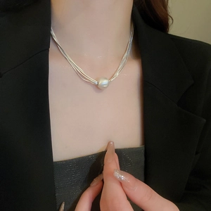Detail view of multi-layer silver snake chain necklace with a large white pearl pendant