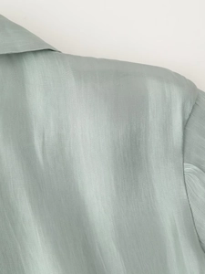 Detail of light green glossy fabric showing bow tie neck and shoulder seam details