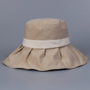 Detail of light khaki sun hat with wide wavy brim and decorative white ribbon band