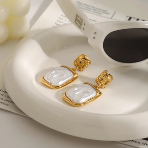 Detail of square gold titanium earrings with pearl inlay on a white ceramic tray