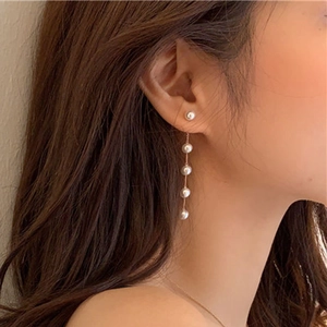 Elegant long gold chain drop earrings with five white pearls worn by a model in a close-up