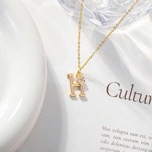 Close-up of gold letter H pendant necklace with zircon flower on magazine page