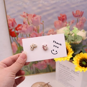 Close-up of asymmetric flower and butterfly earrings on a smiley face earring card