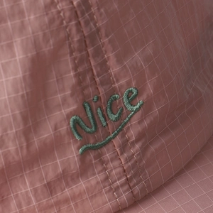 Close-up of pink ripstop fabric texture and green 'Nice' embroidery on baseball cap