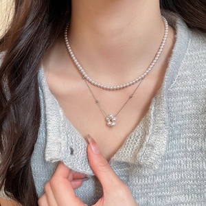 Detail of layered pearl necklace with silver flower pendant on a model wearing grey knitwear