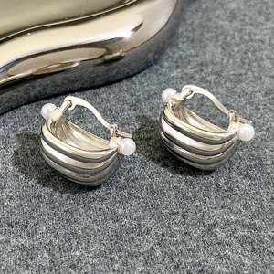 Macro shot of silver metal hoop earrings with pearl accents on grey texture