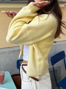 Detail view of a yellow ribbed knit cardigan with buttons in a natural outdoor setting