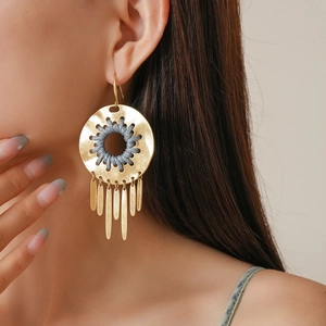 Close-up of gold geometric hollow earrings with leather cord and long metal tassels