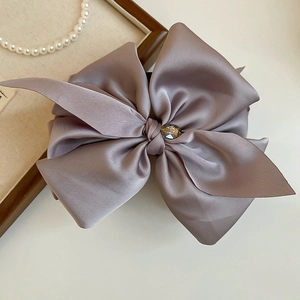 Close-up of a purple satin bow hair claw clip with a luxury crystal center on a table