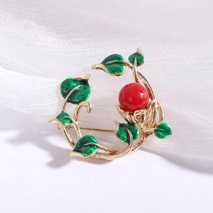 Detail of a gold floral vine brooch with green enamel leaves and a red center bead