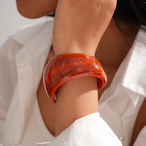 Detail of chunky orange resin bangle with marble texture worn by a model in casual attire