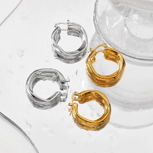 Irregular twisted gold and silver stainless steel hoop earrings on a reflective water surface