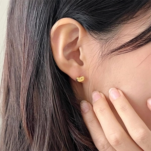 Minimalist golden bean-shaped stud earrings in polished metal finish worn by model
