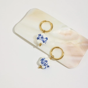 Dettaglio di orecchini placcati oro 18K con ciondoli a fiore in ceramica bianca e blu