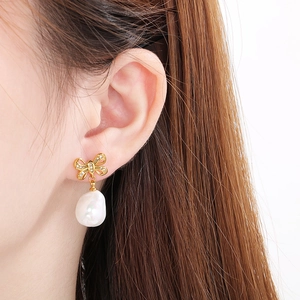 Macro view of gold bow earrings with white baroque pearl drop worn by a model