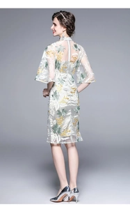 Detail of white embroidered dress with green floral patterns and mesh sleeves on the back