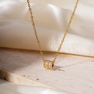Elegant gold cylinder pendant necklace with textured finish on smooth white silk background