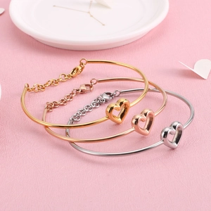Drei minimalistische offene Herzarmreifen in Gold, Roségold und Silber auf Rosa Grund