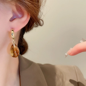 Detail of model wearing gold hoop earrings with amber resin teardrop pendants